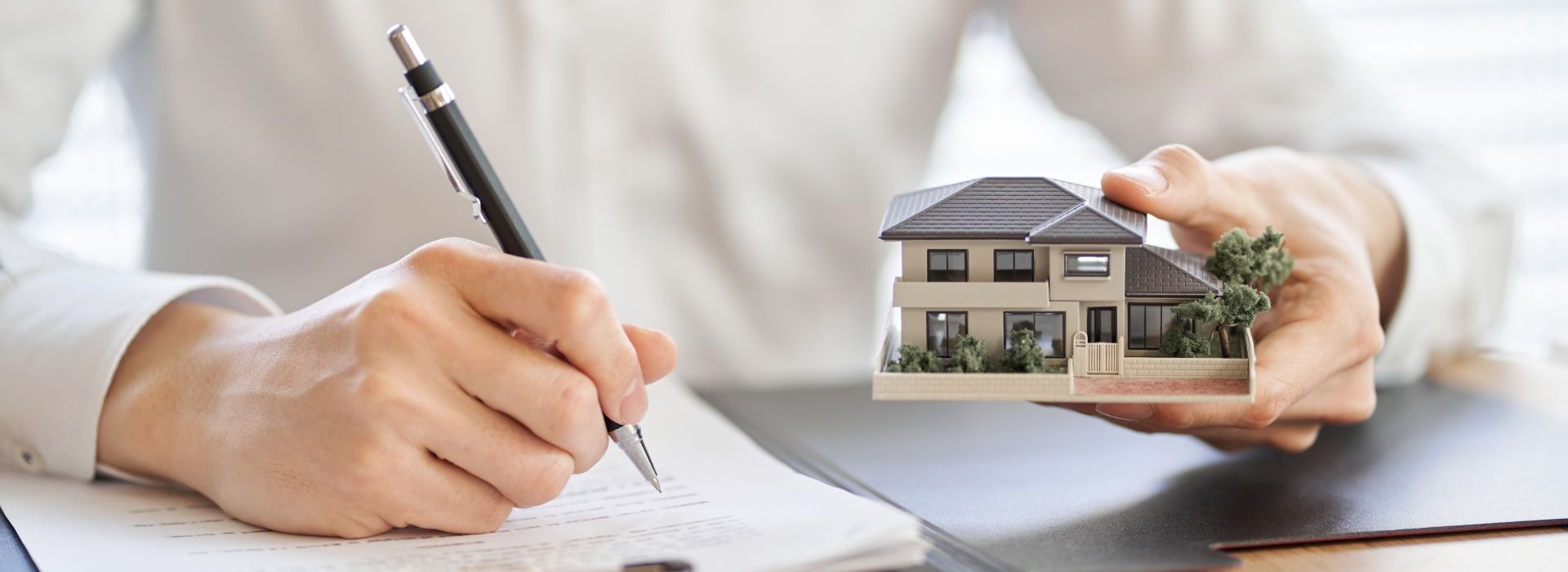 Mann schreibt etwas nieder und hält in der anderen Hand ein kleines Modellhaus