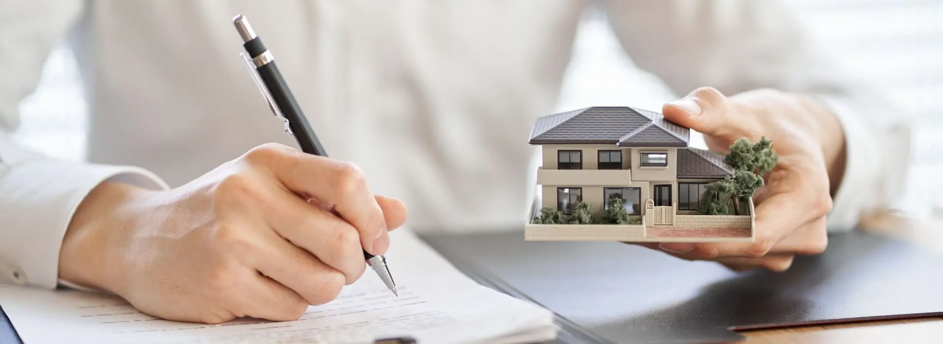 Uomo che scrive qualcosa e tiene nell'altra mano un piccolo modellino di casa