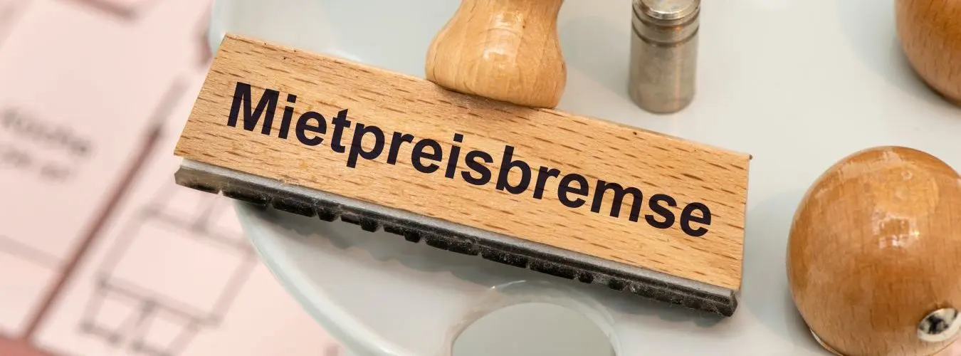 Un timbro di legno con la dicitura Mietpreisbremse sopra la planimetria di un appartamento in affitto